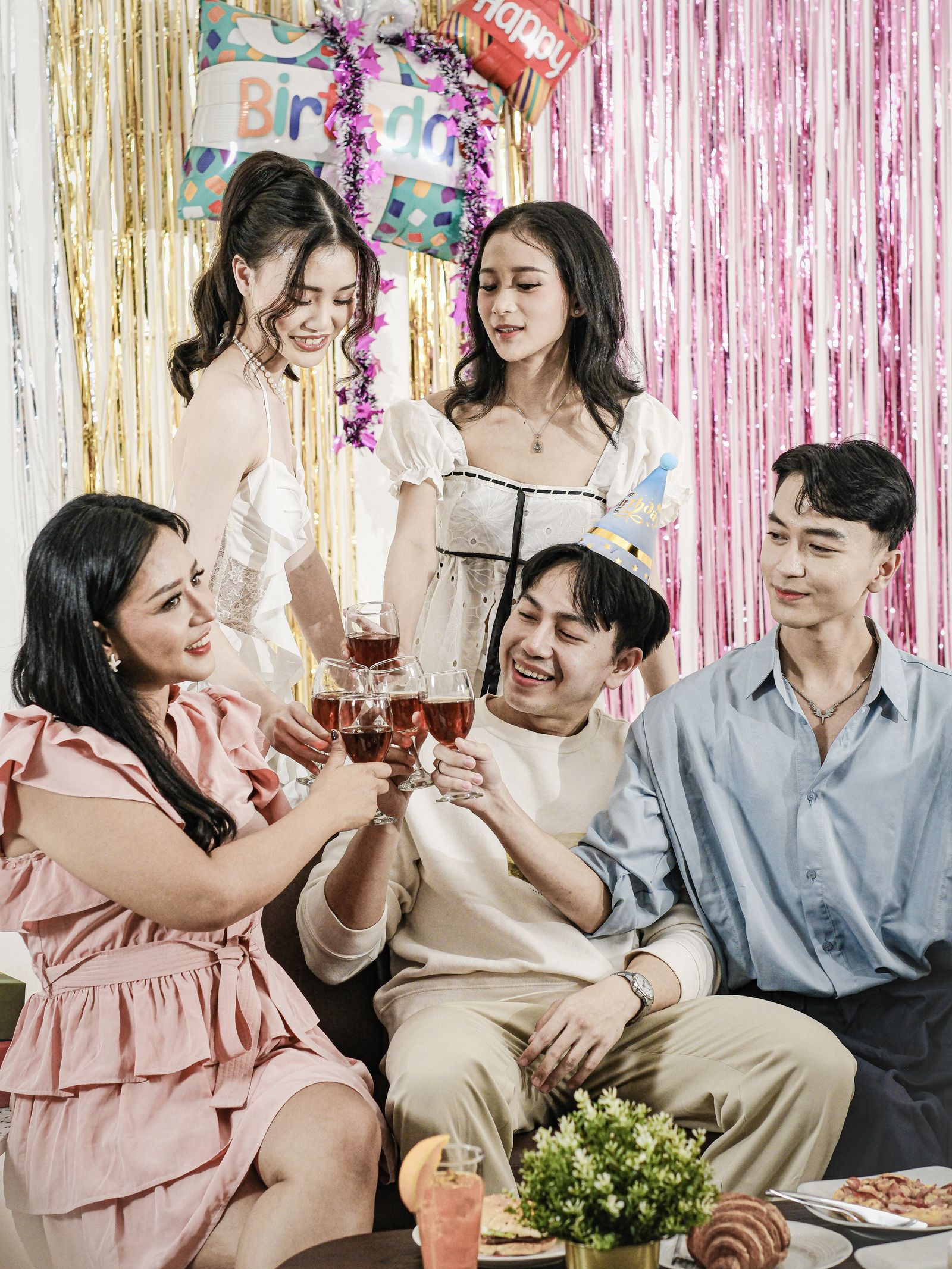 Friends toasting toward the camera in front of a fringe and foil photo booth backdrop