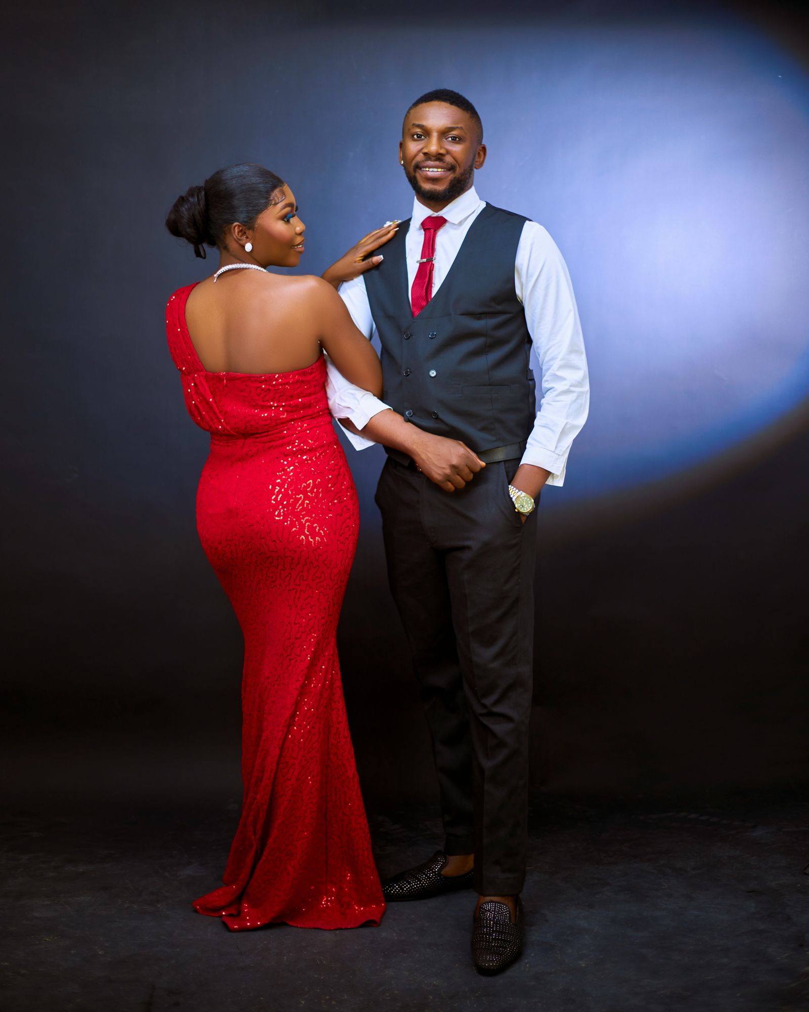 Couple in gown and suit posing for a lit portrait against a dark photo booth backdrop