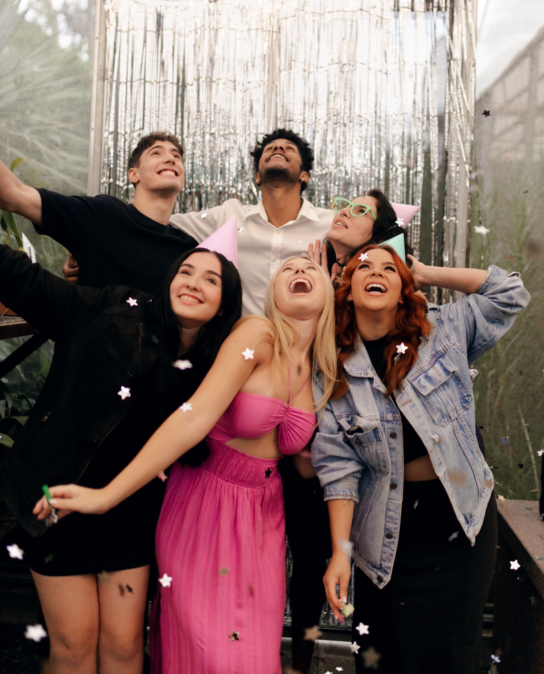 Group of friends posing with party hats in front of a silver fringe photo booth backdrop