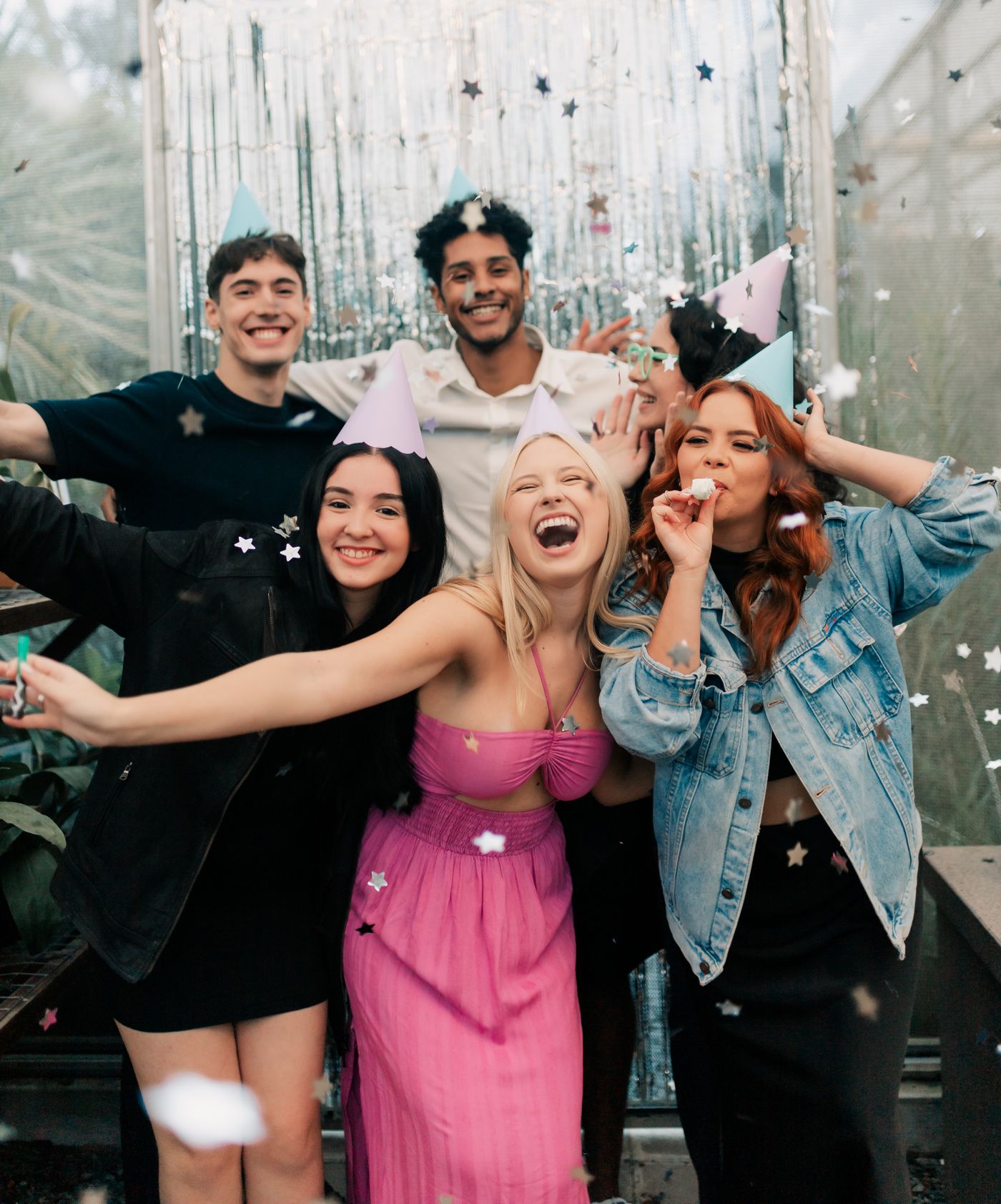 Friends in party hats laughing in front of a silver tinsel photo booth backdrop